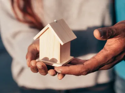 Twee mensen die een klein houte huisje vasthouden Twee mensen die een klein houte huisje vasthouden