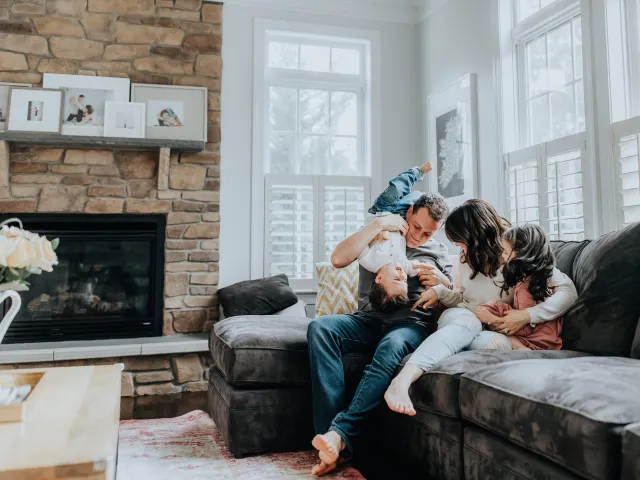des parents et leurs enfants jouent dans le canapé de leur salon.